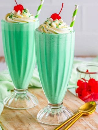 Square image of two Shamrock Shakes topped with whipped cream and cherries.