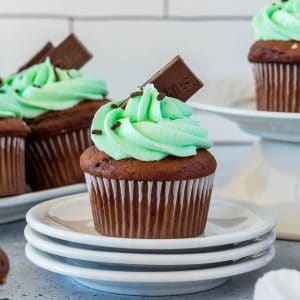 Square image of cupcake garnished with frosting and Andes mint on stacked plates.