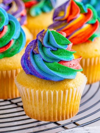 Square image of frosting on cupcakes on wire rack.