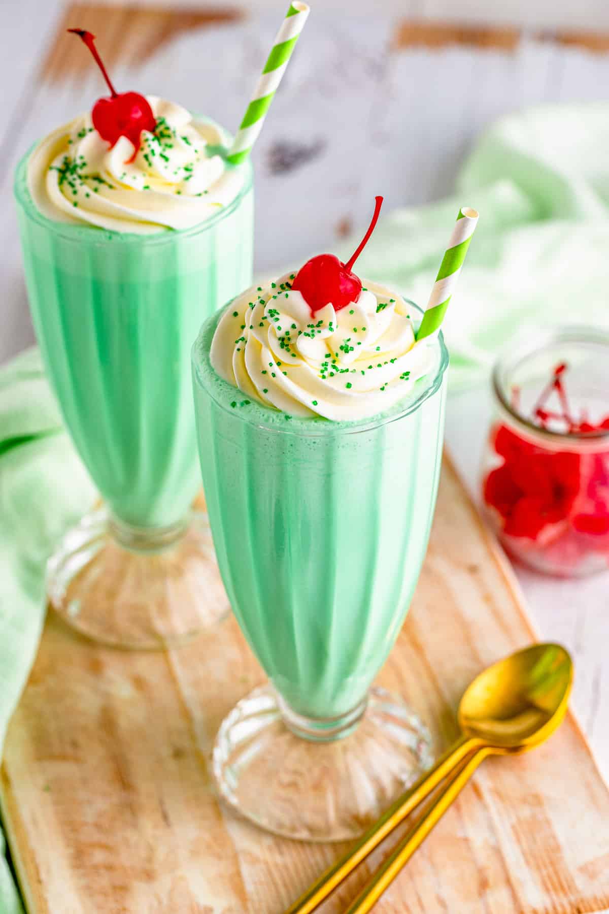 Two of the Shamrock Shake Recipe on wooden board with golden spoon topped with toppings.