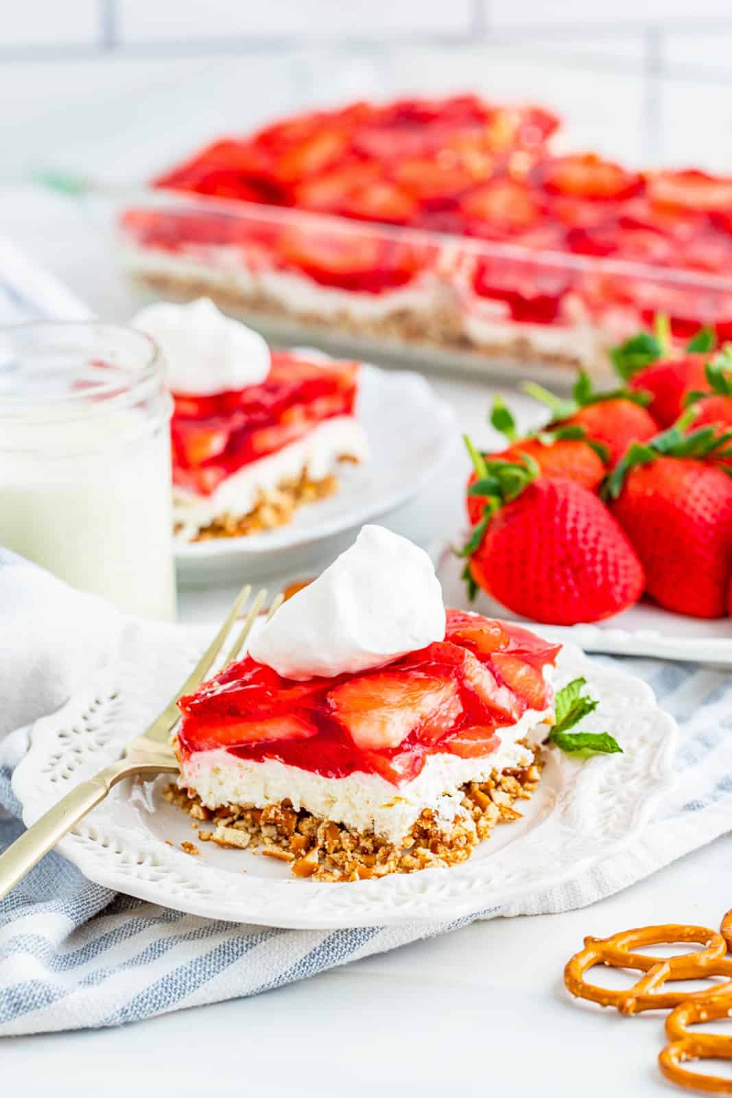 Slice of Strawberry Pretzel Salad on white plate with milk and strawberries beside it.