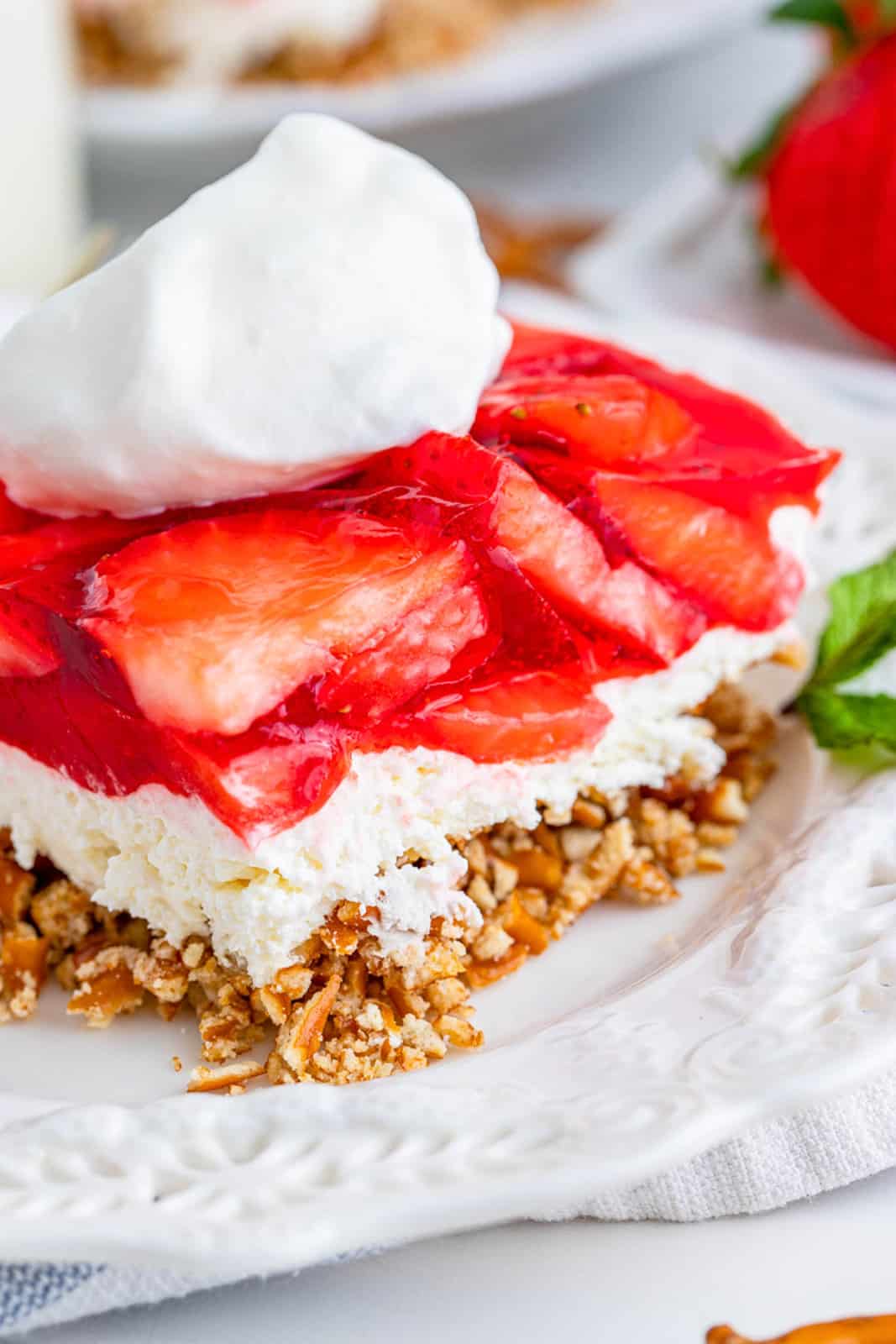Close up side image of layers of Strawberry Pretzel Salad on white plate topped with whipped cream.
