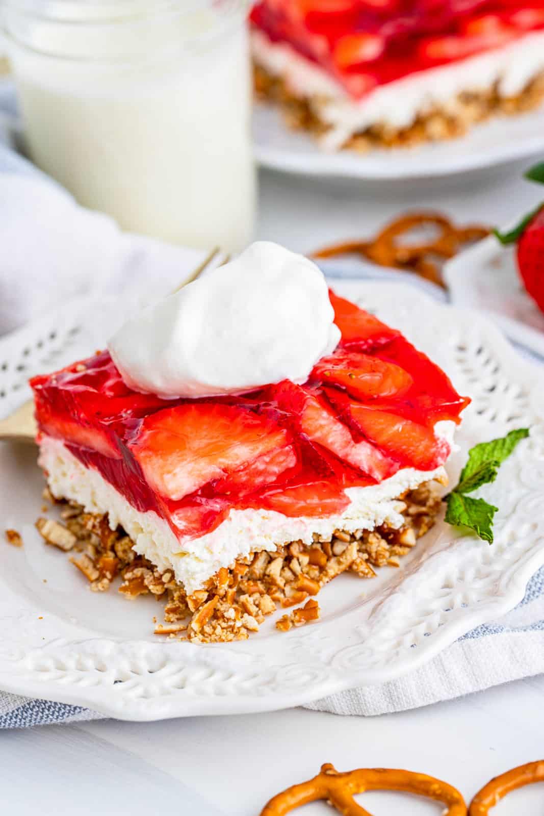 Slice of Strawberry Pretzel Salad on white plate with mint and whipped cream.