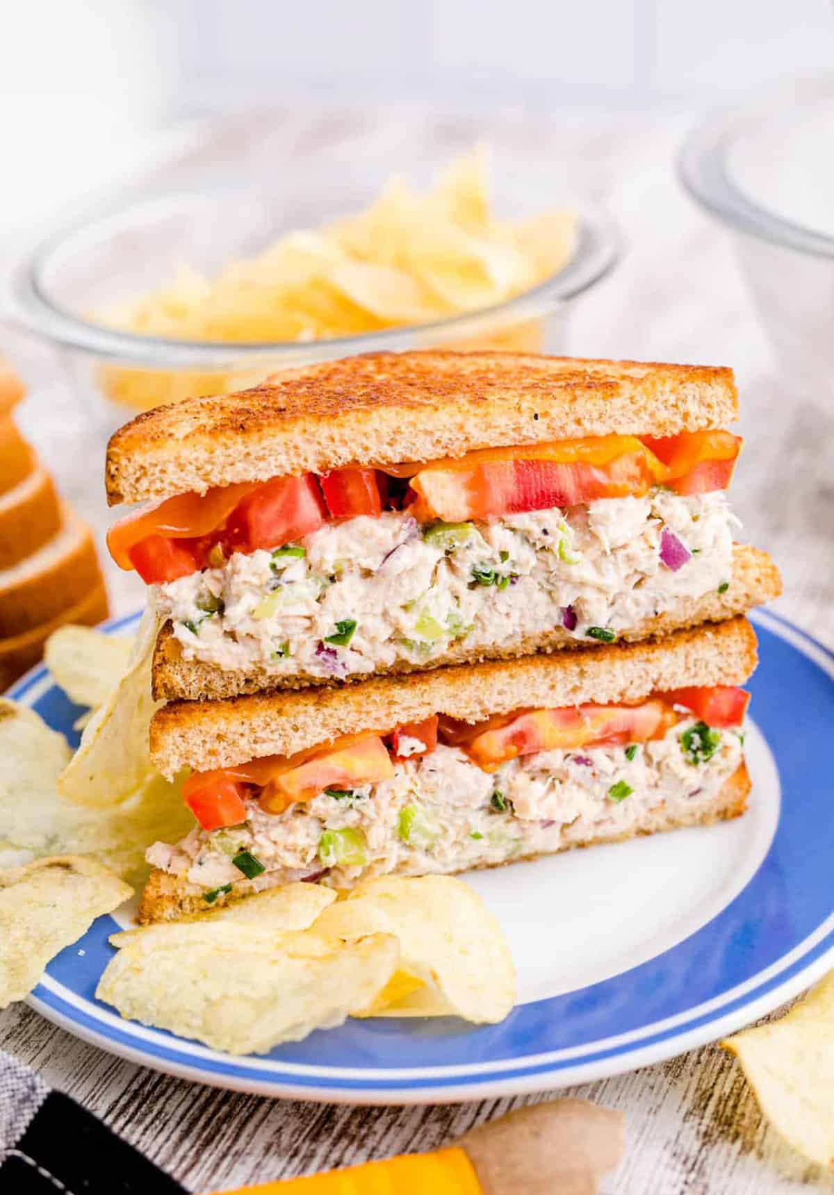 Tuna Melt Recipe cut in half on white and blue plate served with potato chips.