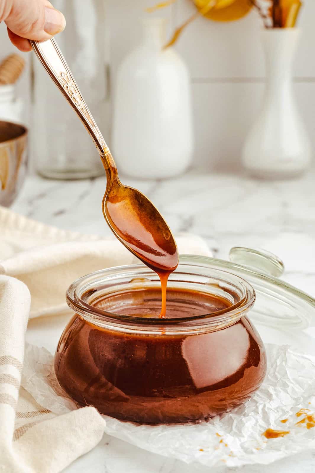 Bourbon Caramel Sauce in jar with spoon dripping sauce.