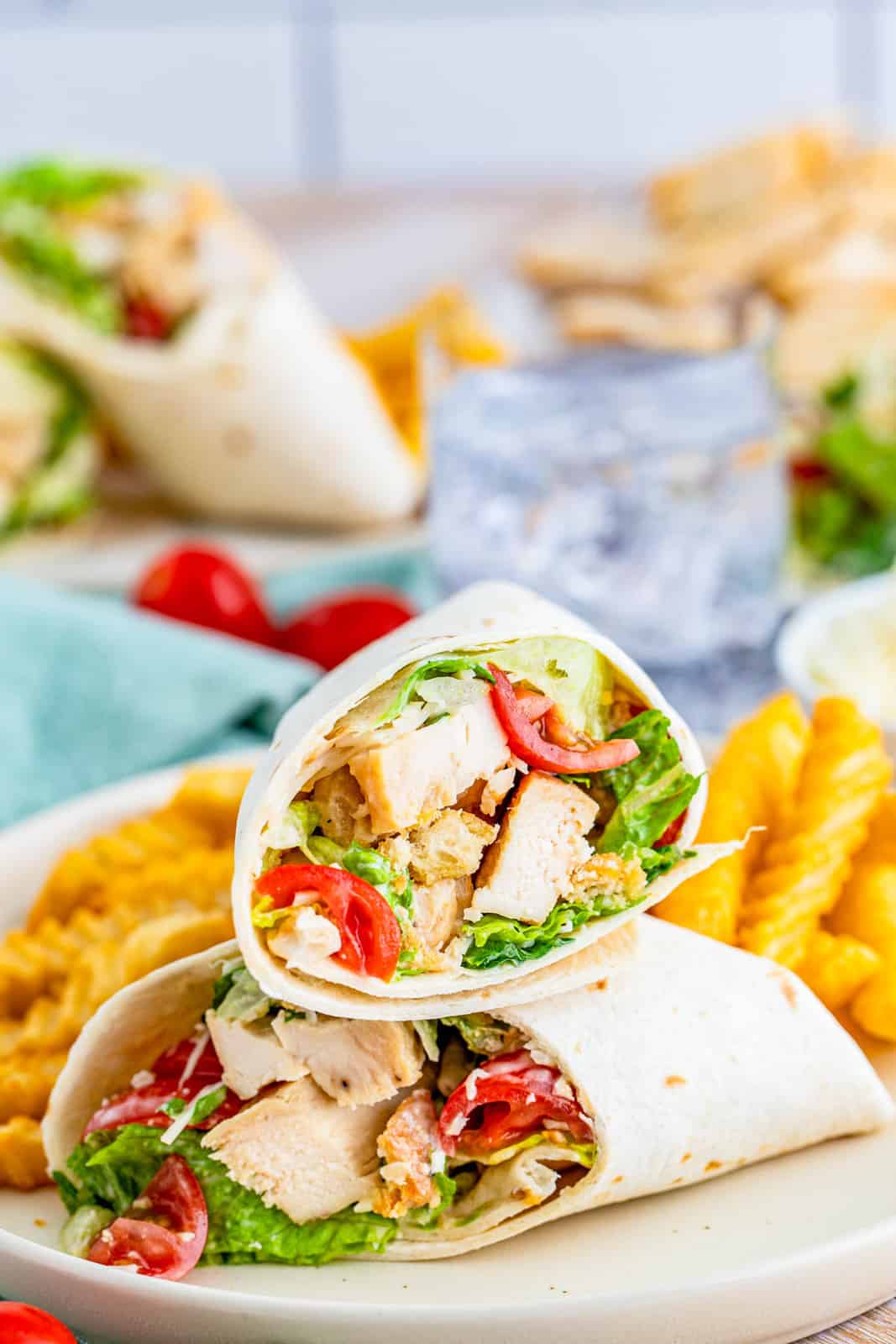 Stacked Chicken Caesar Wraps cut in half on top one one another on plate with fries.