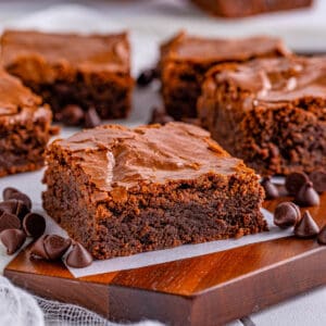 Square image of brownies on wooden board on parchment paper.