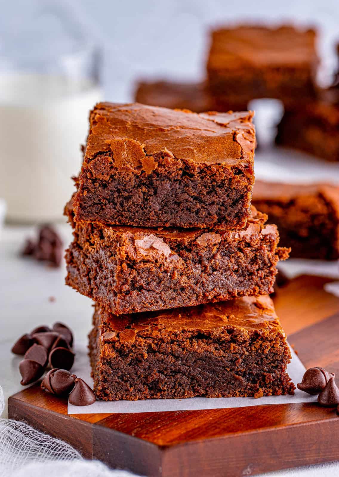 Three stacked Fudge Brownies on parchment paper with chocolate chips by them.