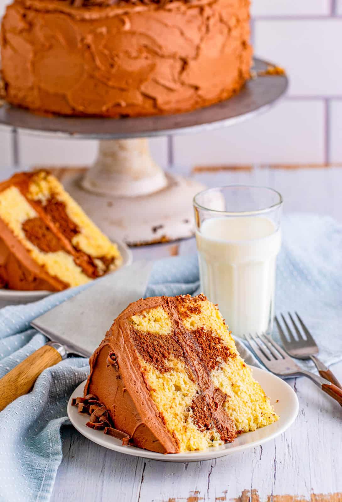 Two slices of Marble Cake Recipe on white plate with whole cake and milk in background.