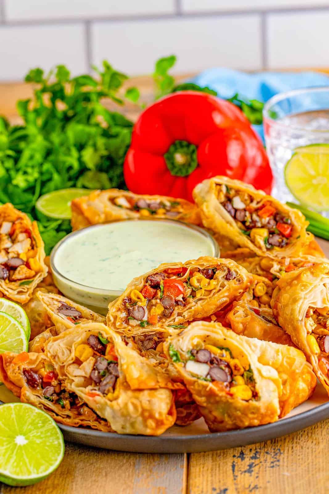 Stacked Southwest Egg Rolls on platter with dipping sauce and garnishes.