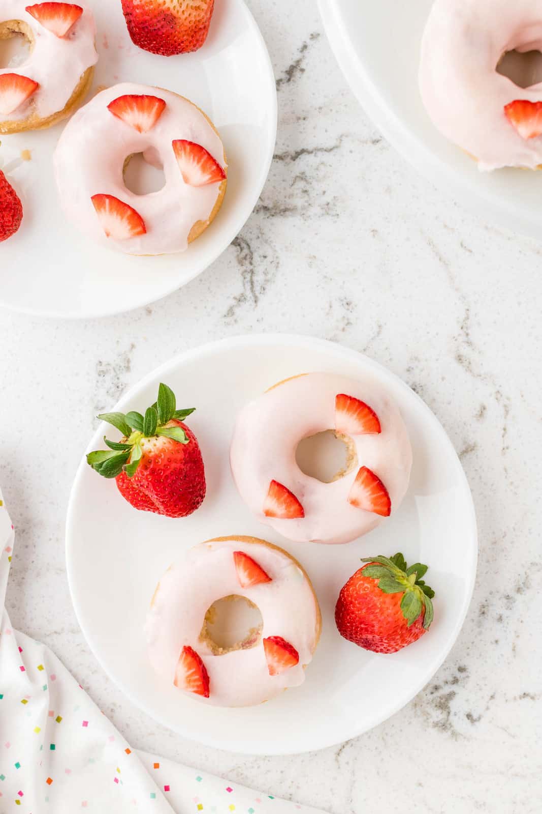 Overhead of two plates with Strawberry Donuts with slices of strawberry on them.