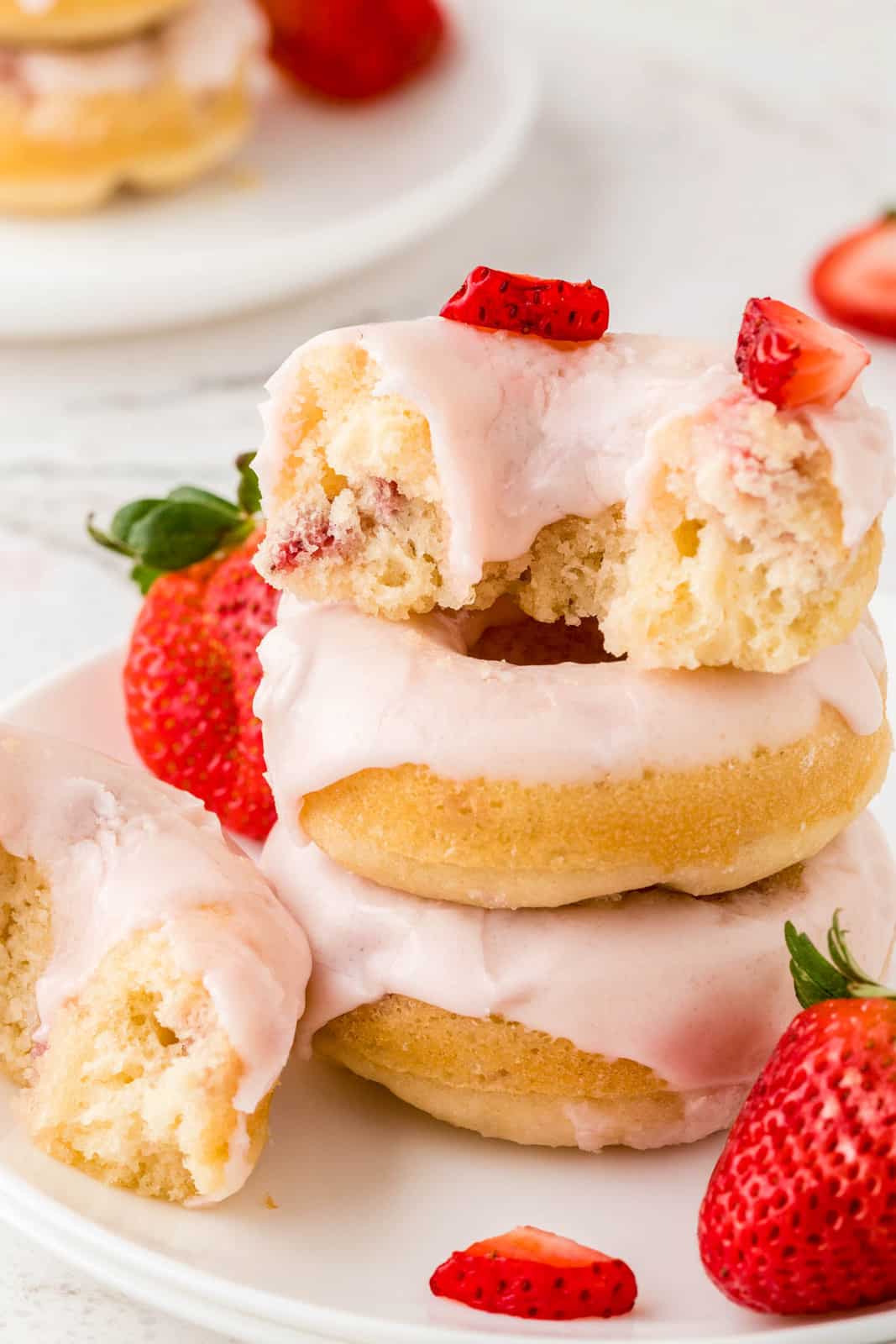 Stacked Strawberry Donuts with top one broken in half showing inside.