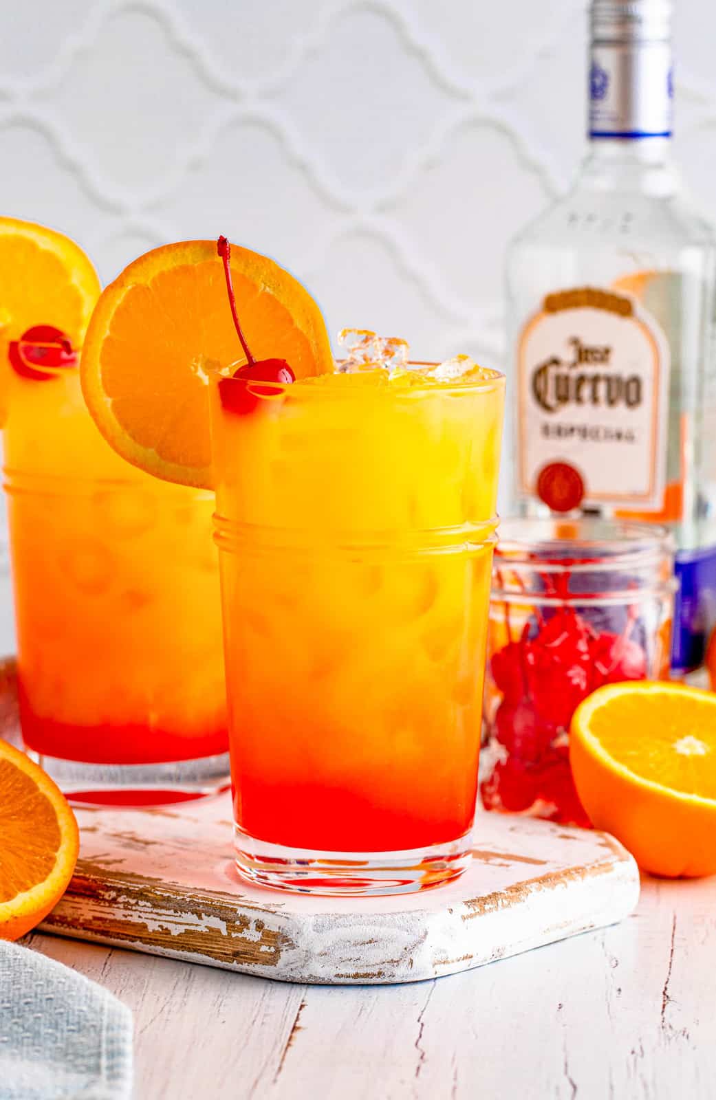 Two glasses of the Tequila Sunrise Recipe with bottle of tequila in back.