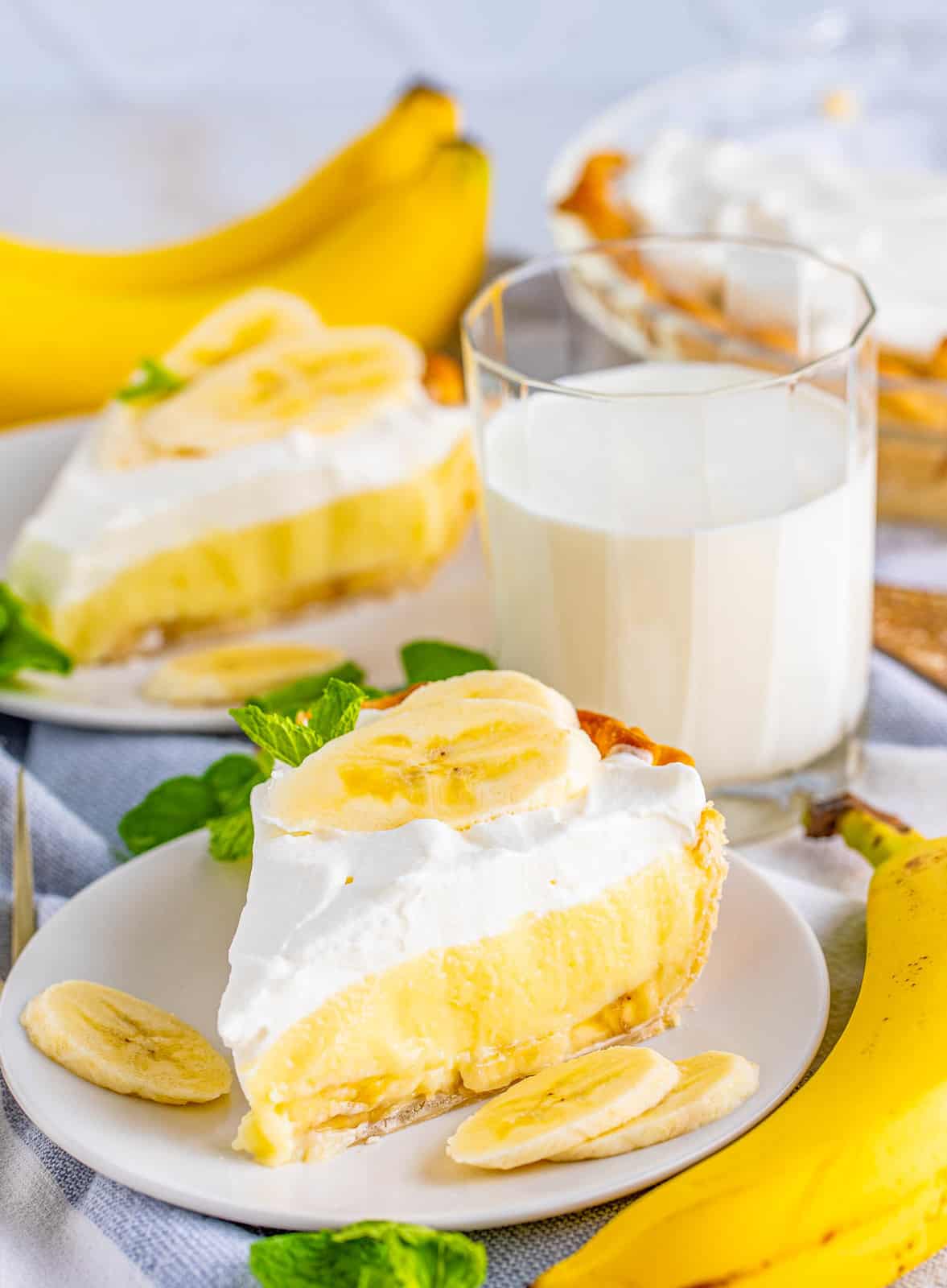 Two slices of Banana Cream Pie on white plates with milk in background.