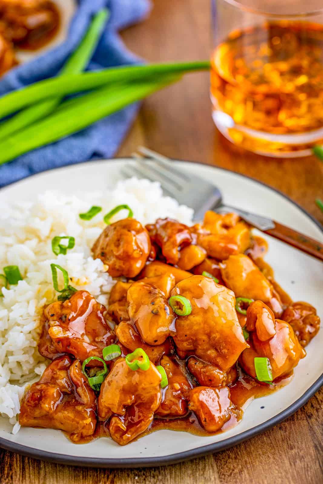 Close up of garnished Bourbon Chicken on white plate with rice and green onions.