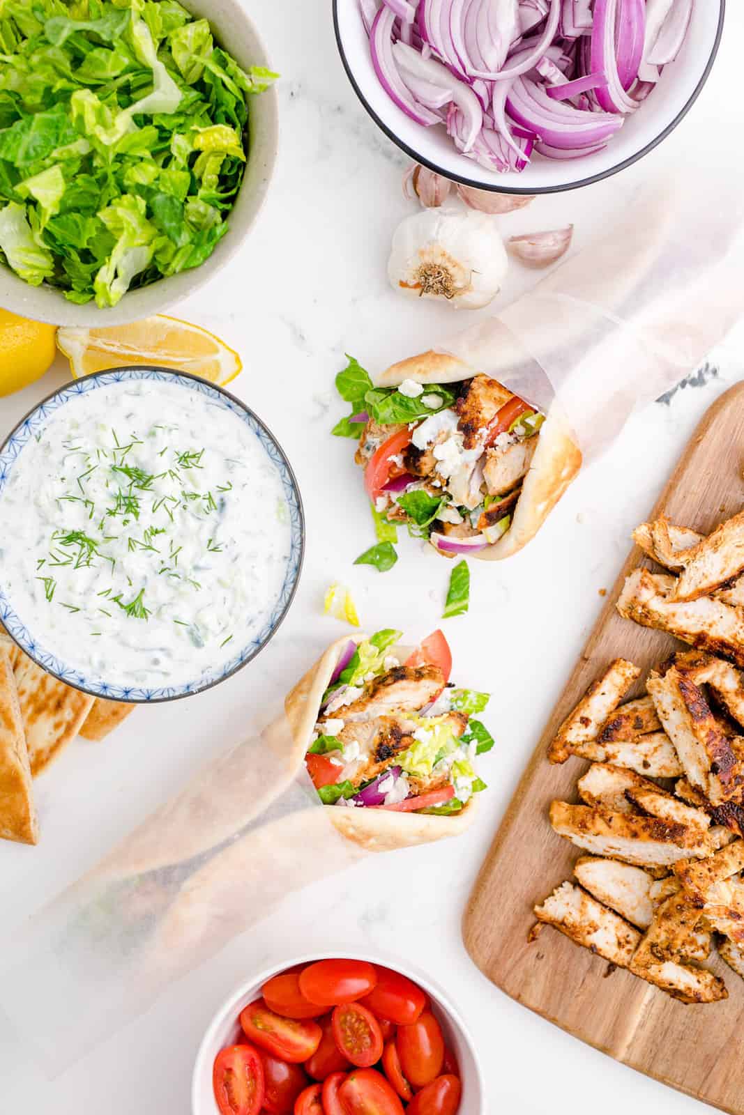 Overhead of two Chicken Gyros with tzatziki sauce and other ingredients.