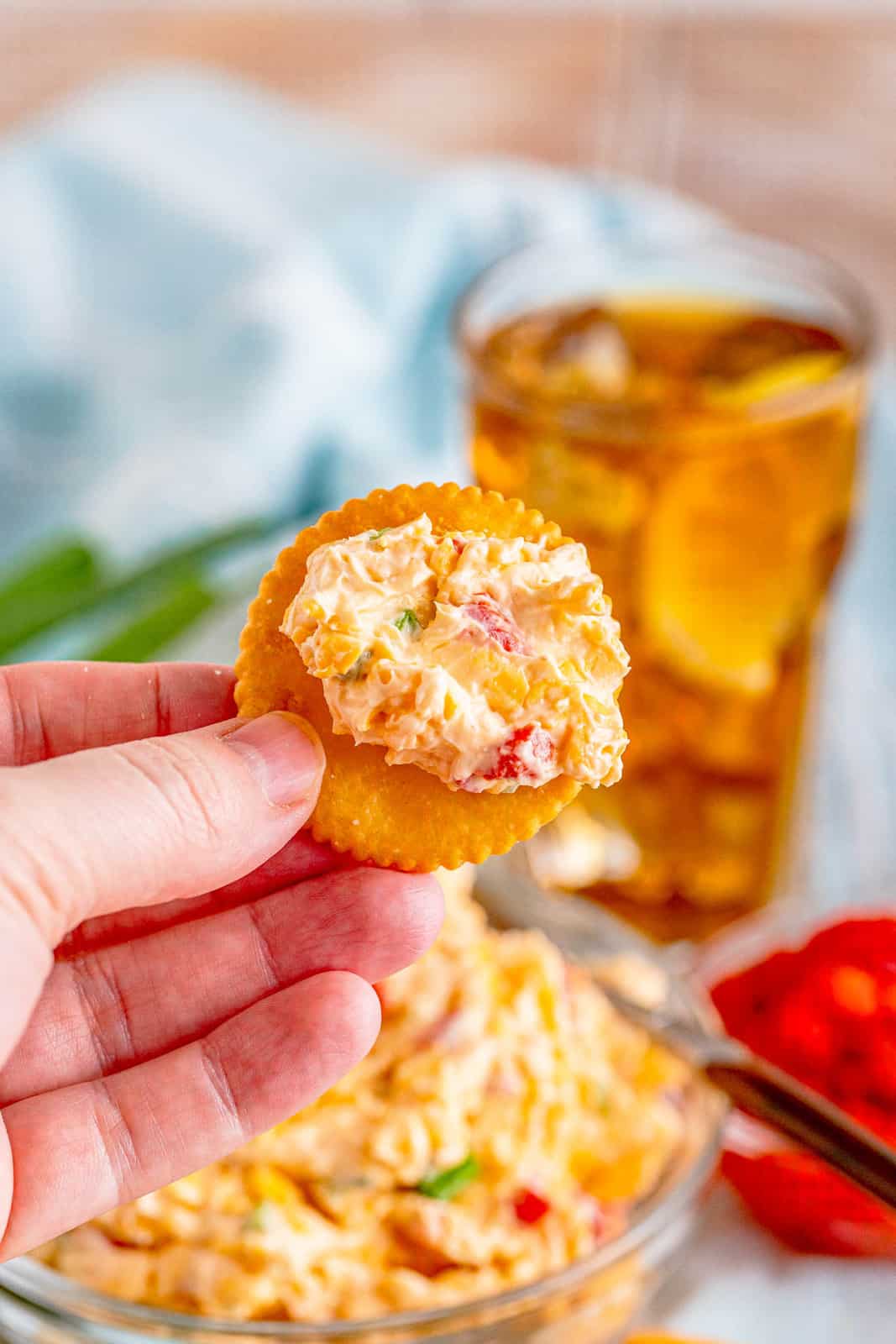 Hand holding up cracker with some Pimento Cheese on it.
