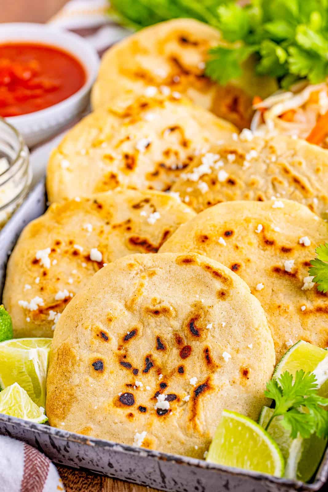 Close up of layered Pupusas in metal tray with garnishes.