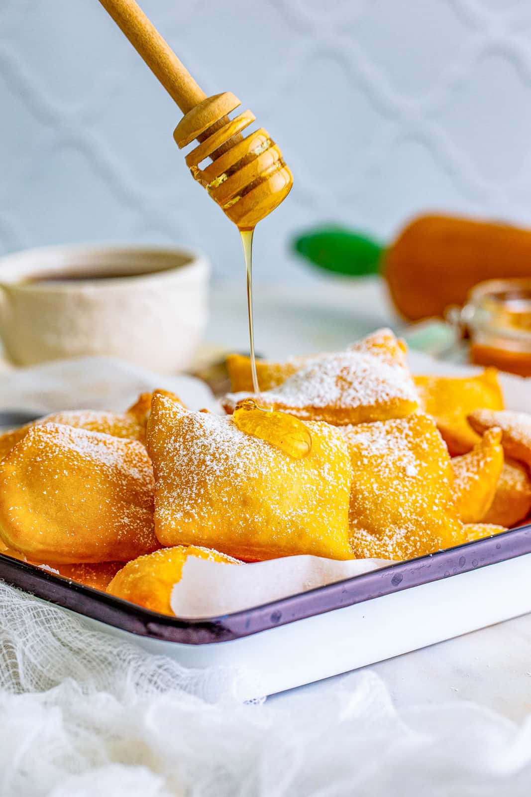 Honey being drizzled over Sopapillas on platter with powdered sugar.