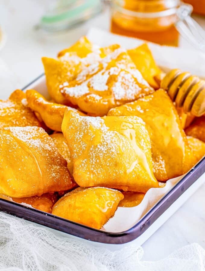 Square image of Sopapilla Recipe on tray with powdered sugar and honey.