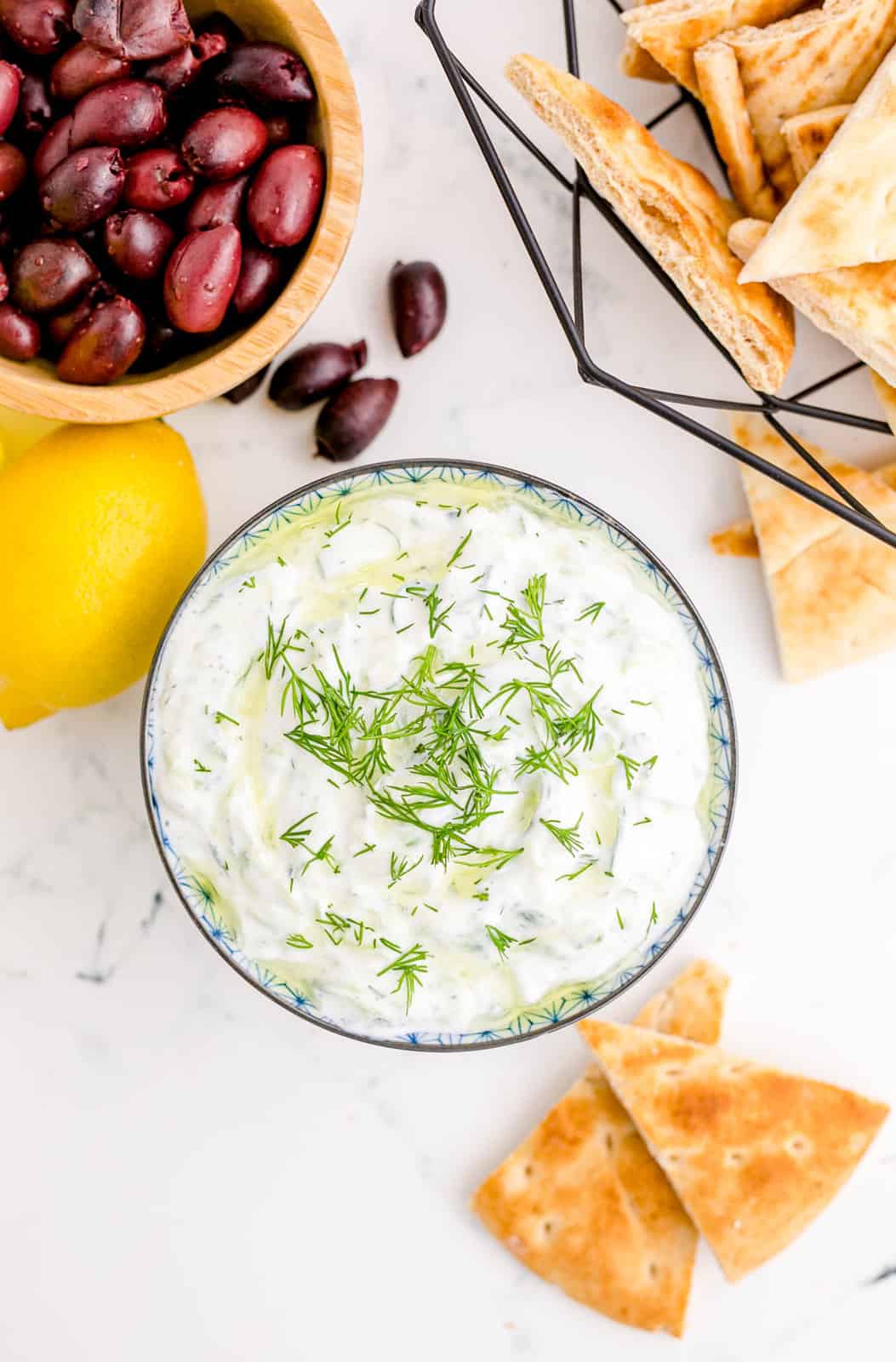 Overhead of Tzatziki Sauce in bowl with pita and olives.