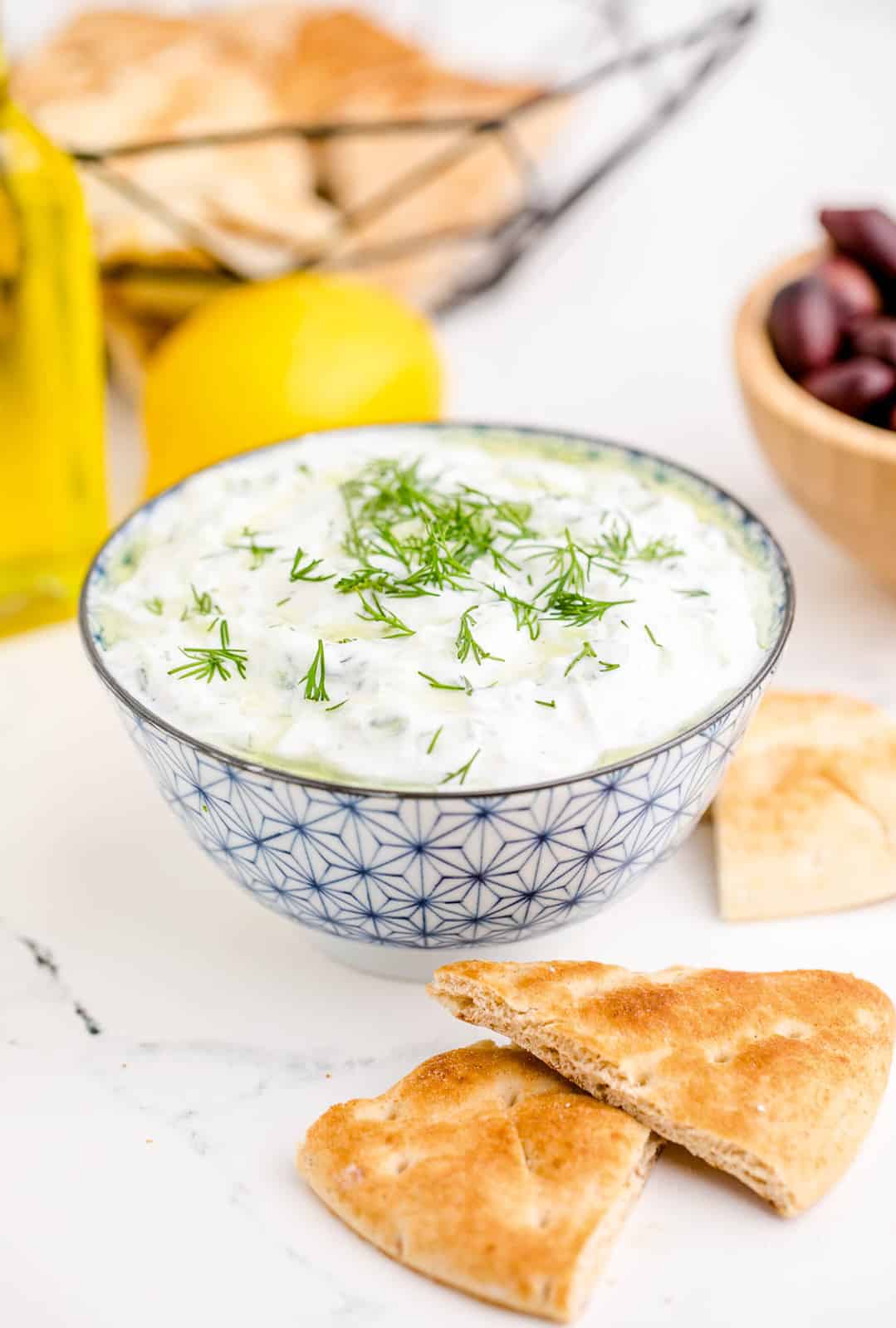 Finished Tzatziki Sauce in bowl with dill and pita bread around bowl.