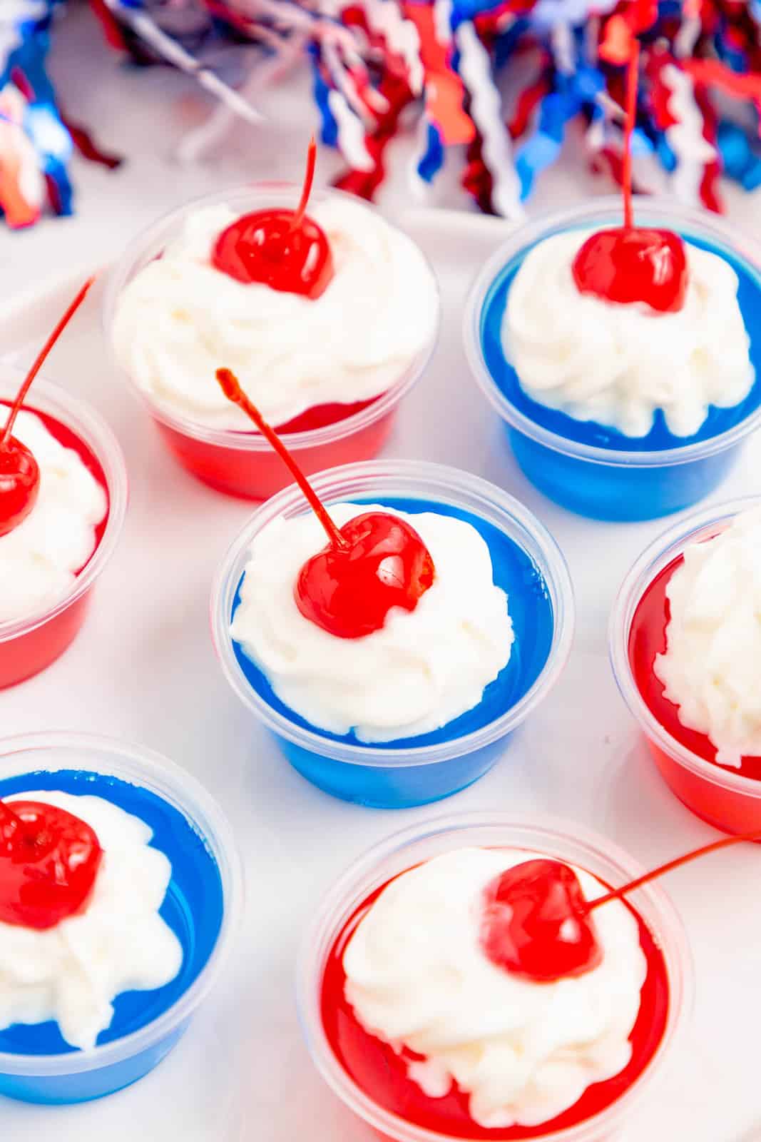 4th of July Jello Shots lined up topped with whipped cream and cherry garnish.