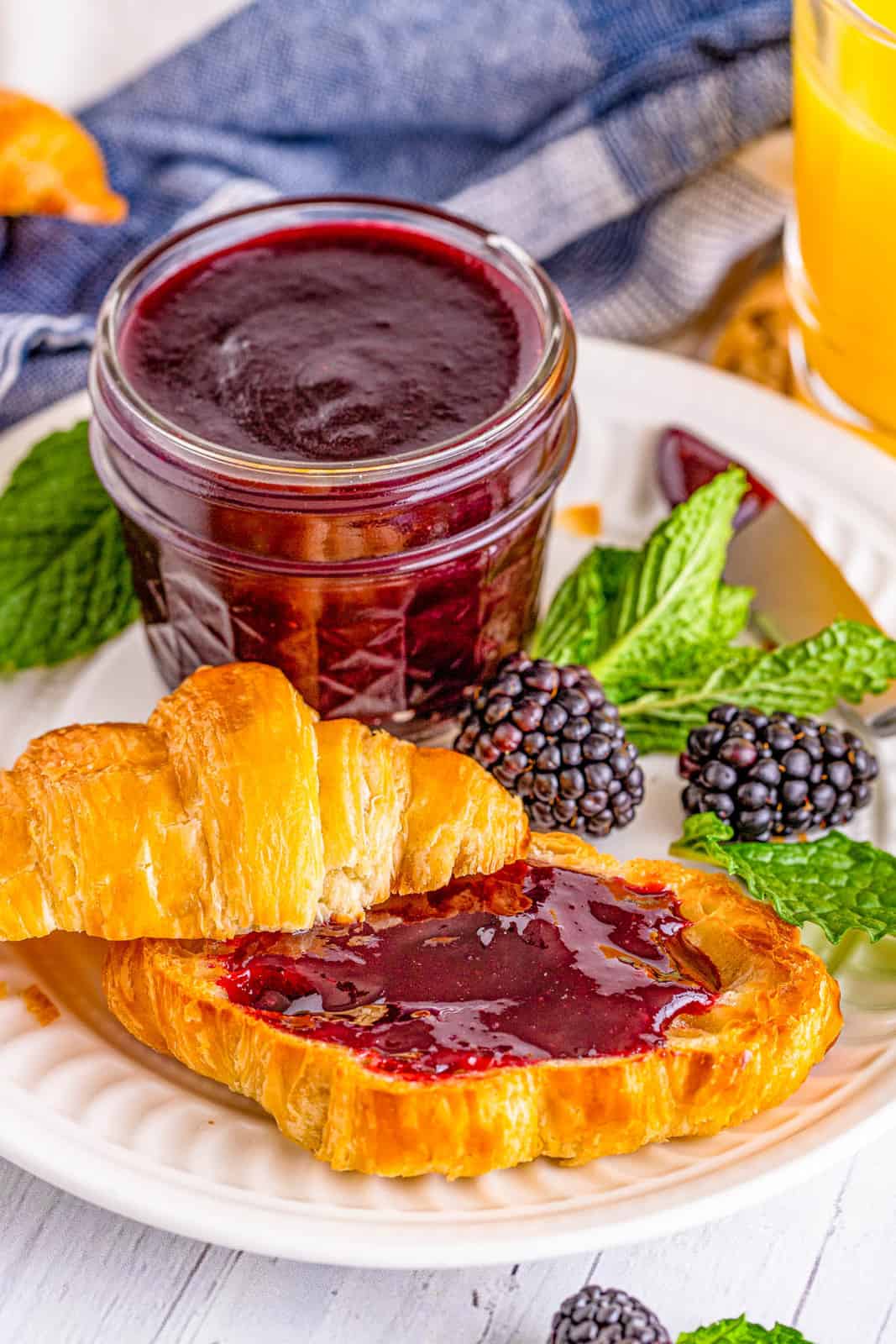 Plate with a croissant spread with Blackberry Jam and jar of jam on plate as well.