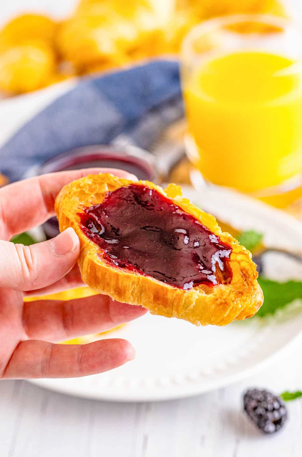 Hand holding up a croissant spread with Blackberry Jam.