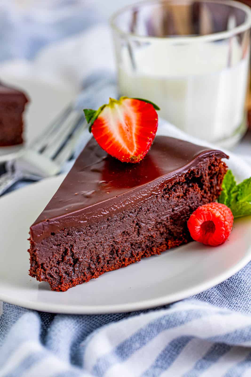 Slice of Flourless Chocolate Cake on white plate with strawberry garnish.