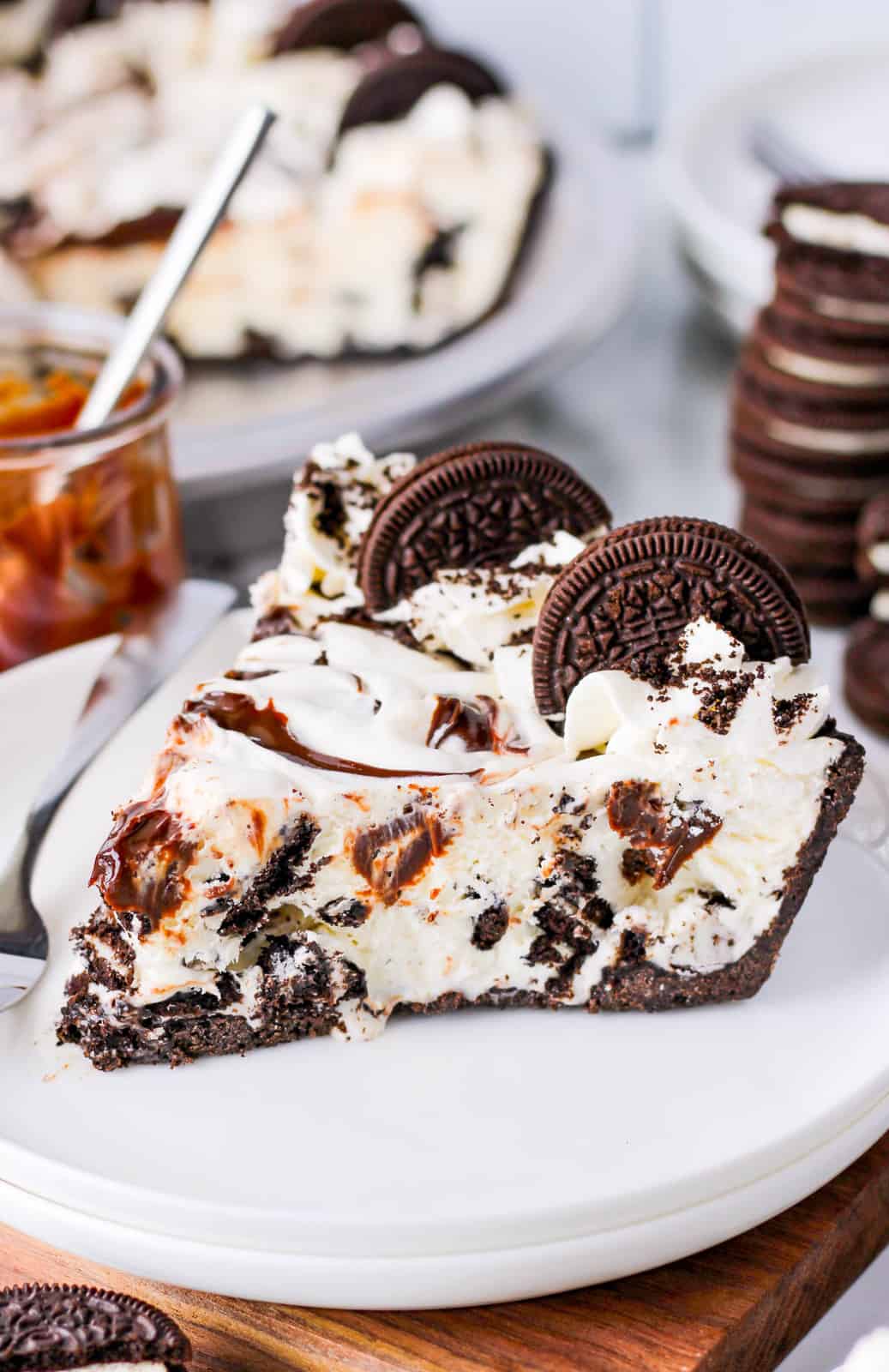 Slice of Oreo Ice Cream Pie on white plate garnished with oreos and whipped cream.