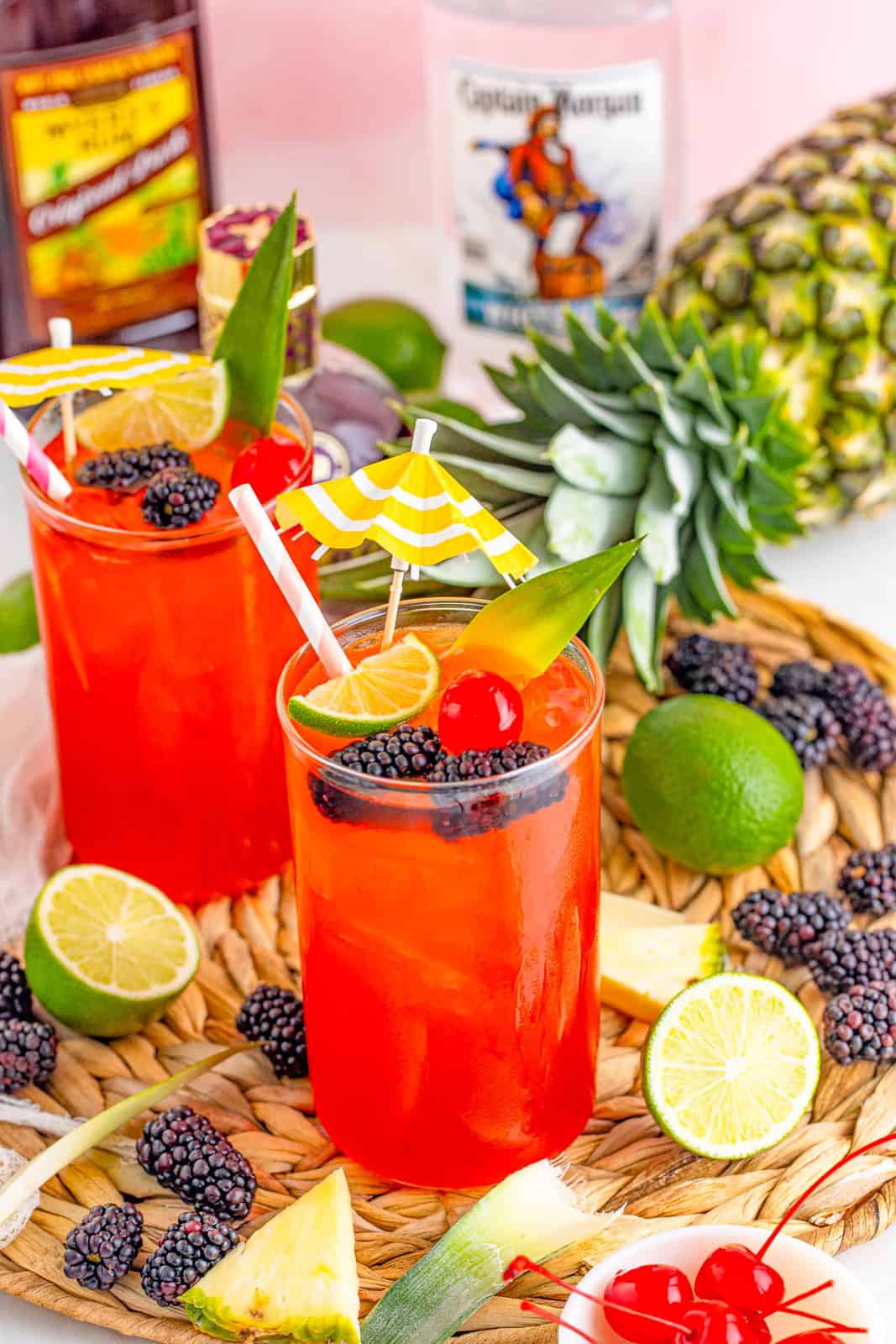 Two Rum Runner Cocktails on wicker tray with fruit and garnishes.