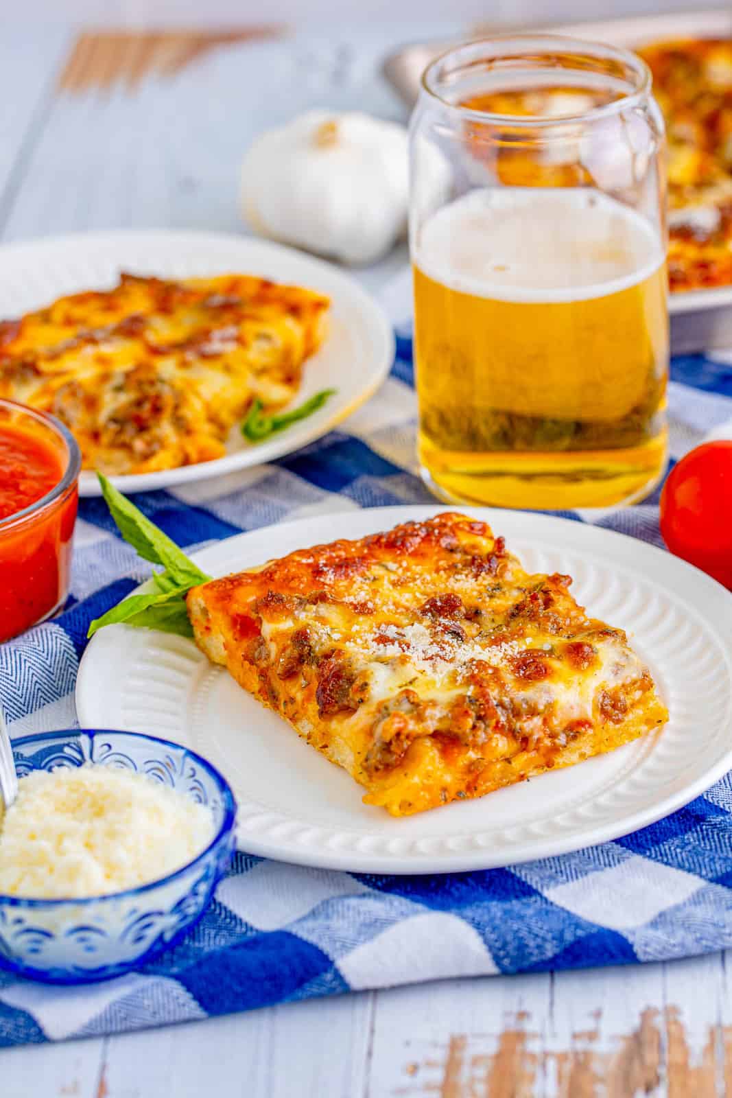 Two slices of Sheet Pan Pizza on white plates with beer in background.