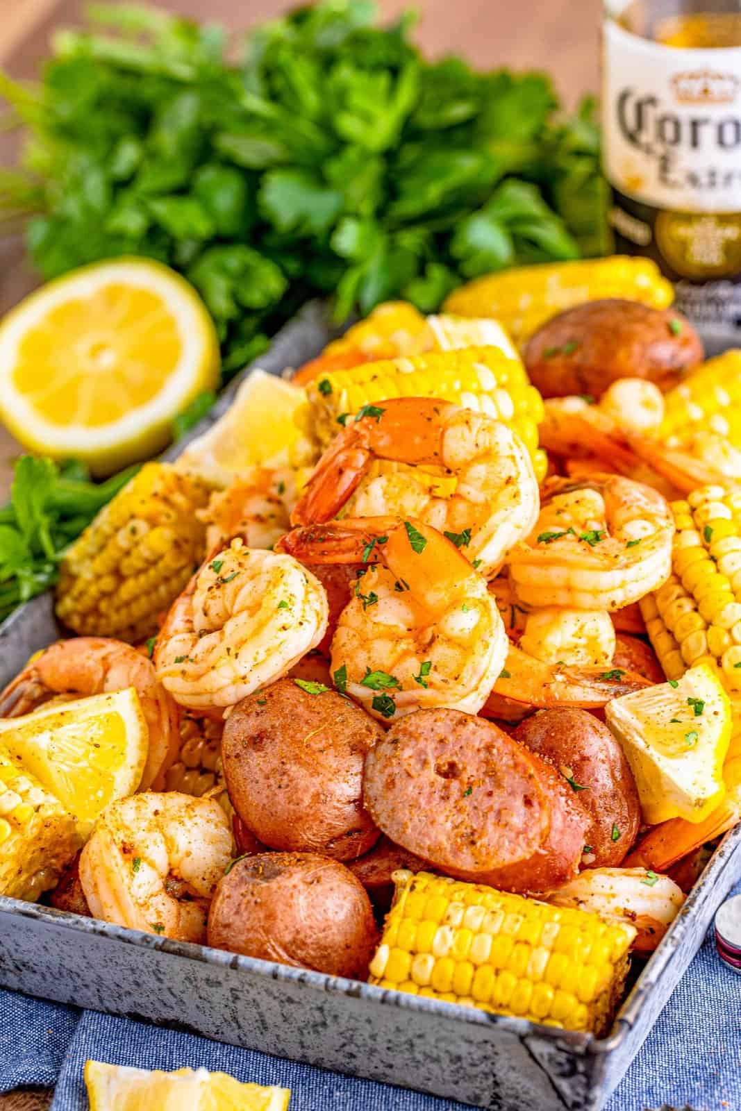 Shrimp Boil Recipe layered on a metal tray with lemon, parsley and beer in background.