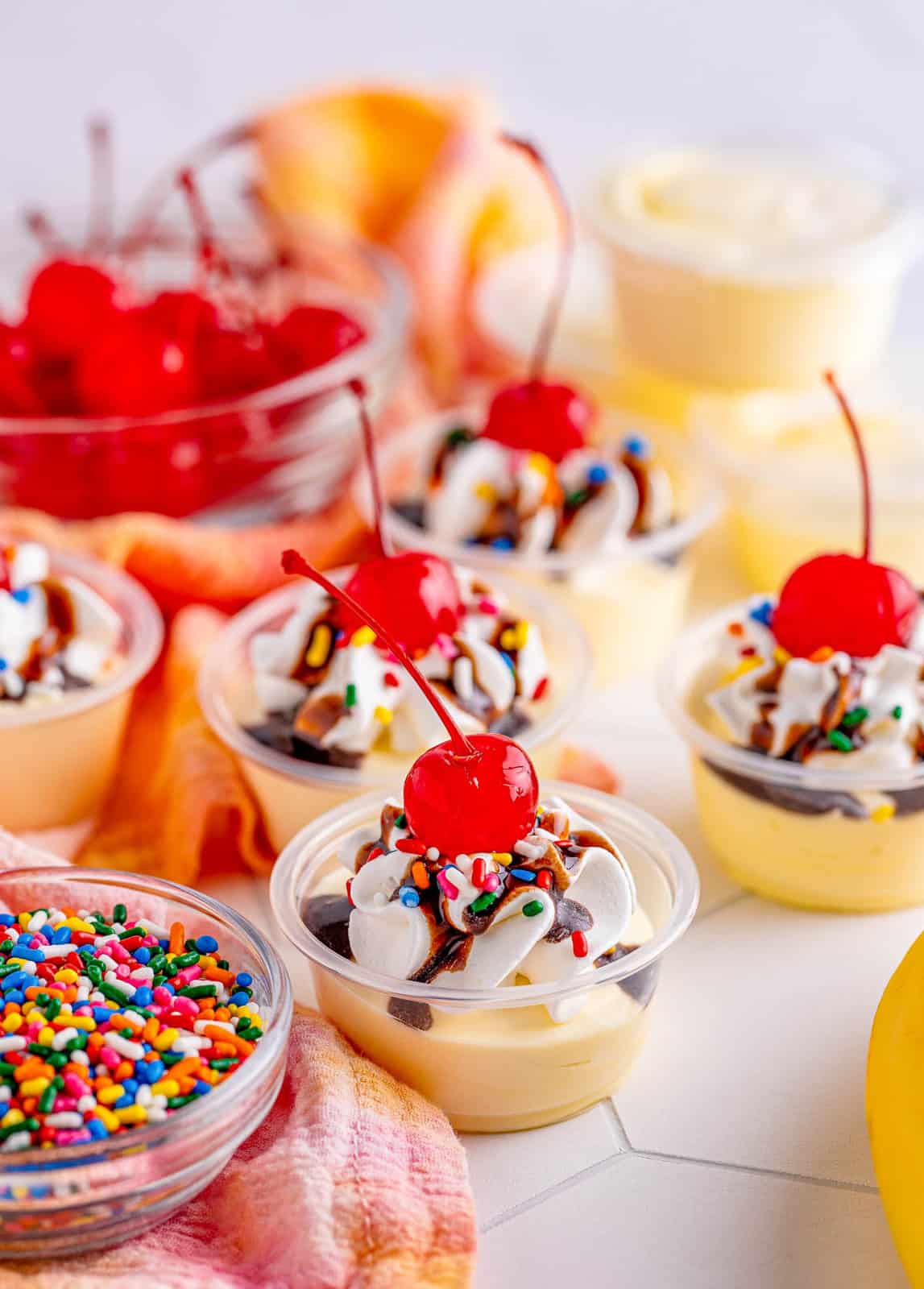 Banana Split Pudding Shots garnished with sprinkles and cherries around them.
