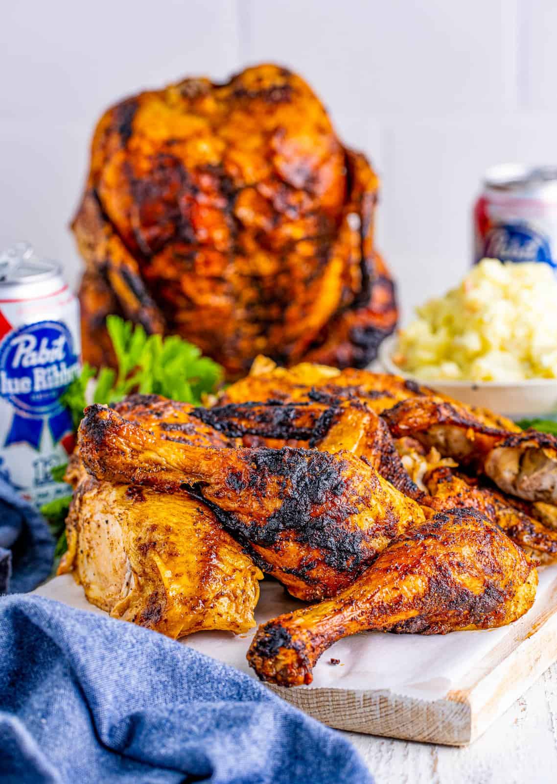 Beer Can Chicken pieces on white board with whole chicken and beer can in background.