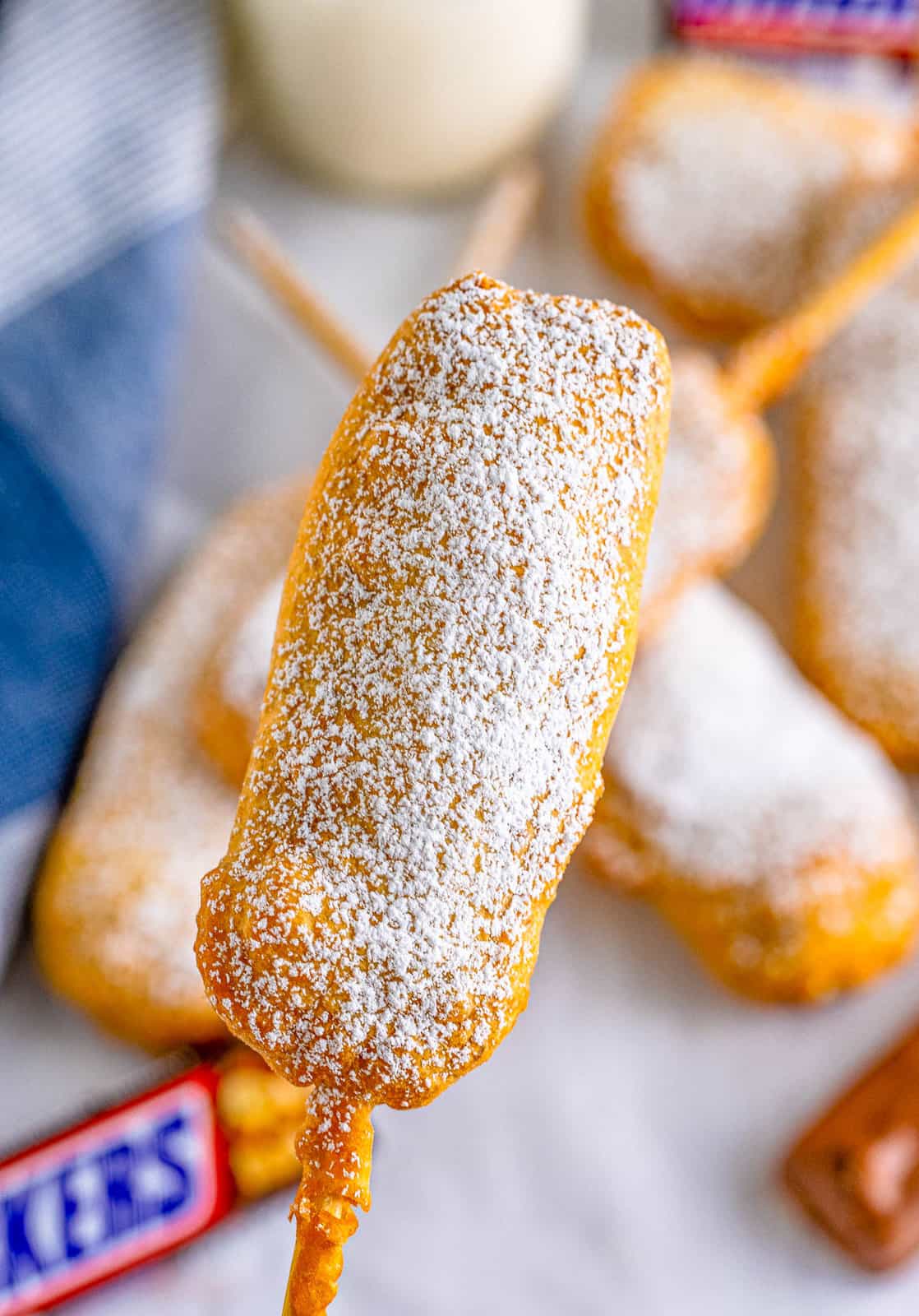 Hand holding up one Deep Fried Snickers showing powdered sugar.