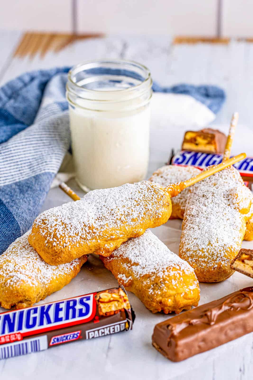 Stacked Deep Fried Snickers on parchment paper covered in powdered sugar with milk and snickers bars.