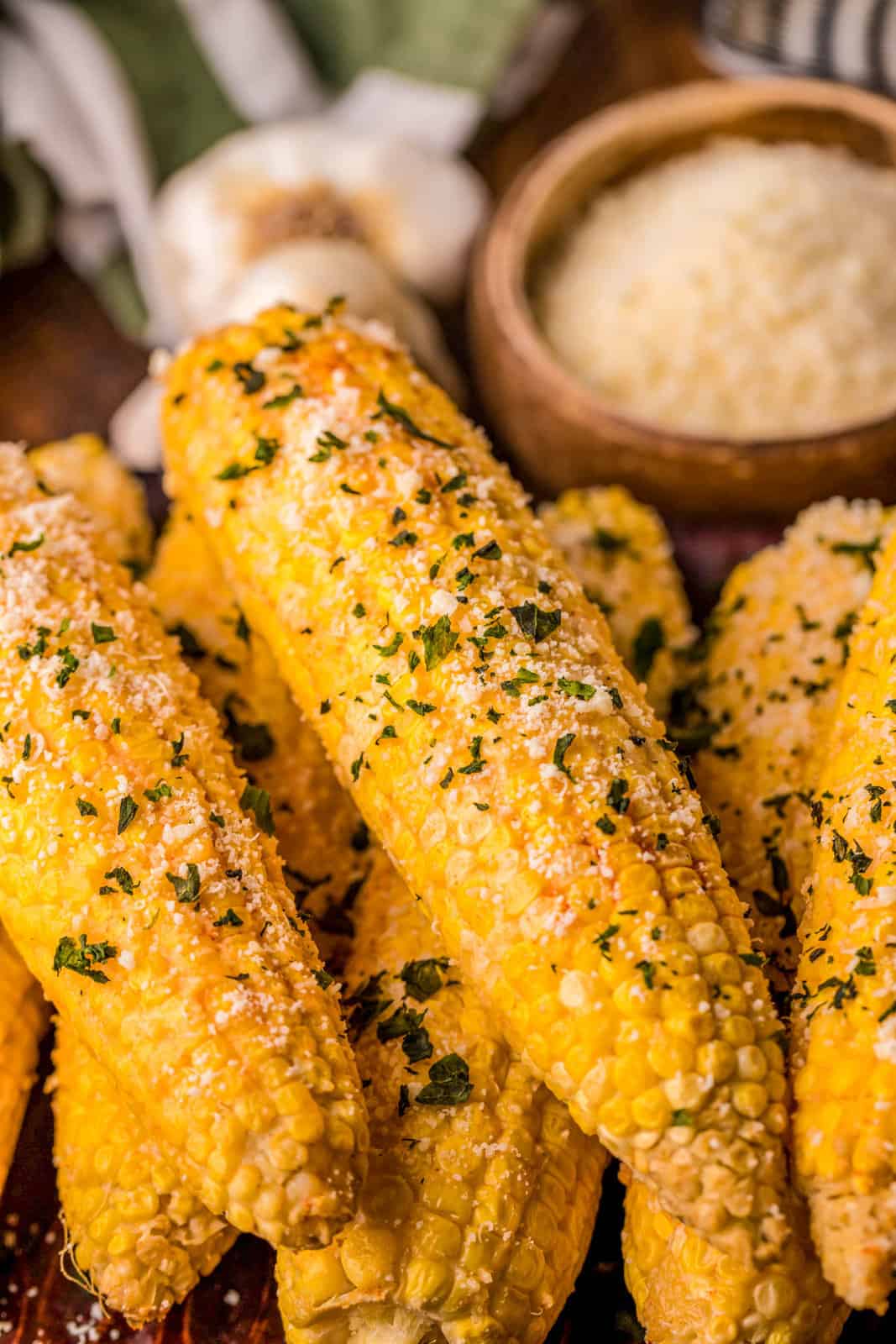 Stacked garnished Smoked Corn on the Cob with cheese in background.