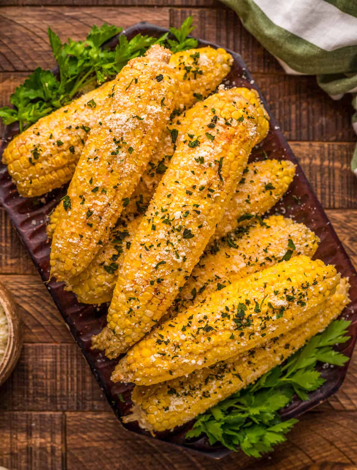 Overhead of Smoked Corn on the Cob stacked on wooden platter, garnished.