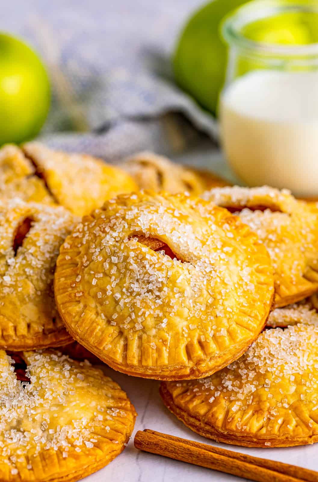 Stacked Apple Hand Pies with cinnamon stick, milk and apples in background.