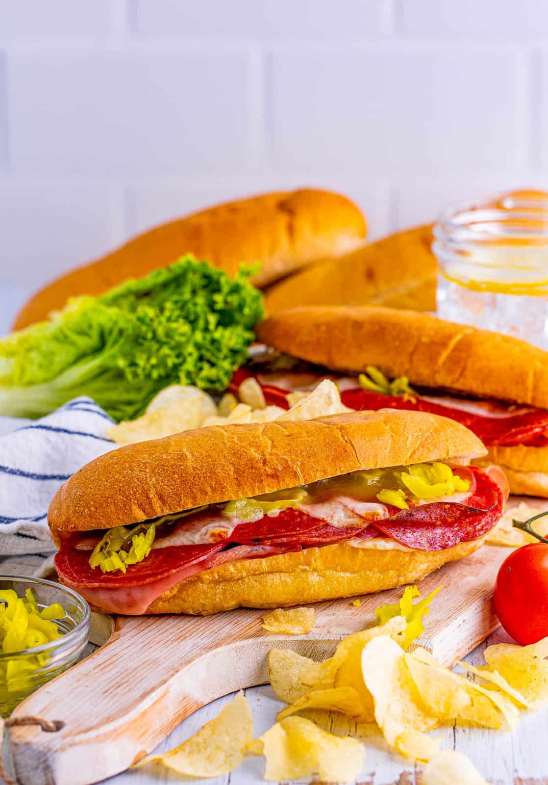 Baked Italian Subs on wooden board with ingredients on it.