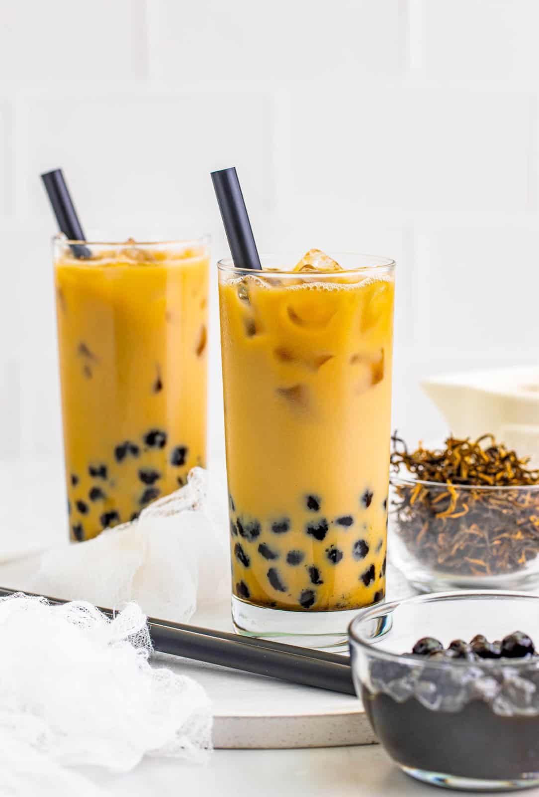 Two glasses of Bubble Tea Recipe with straws and ingredients in background.