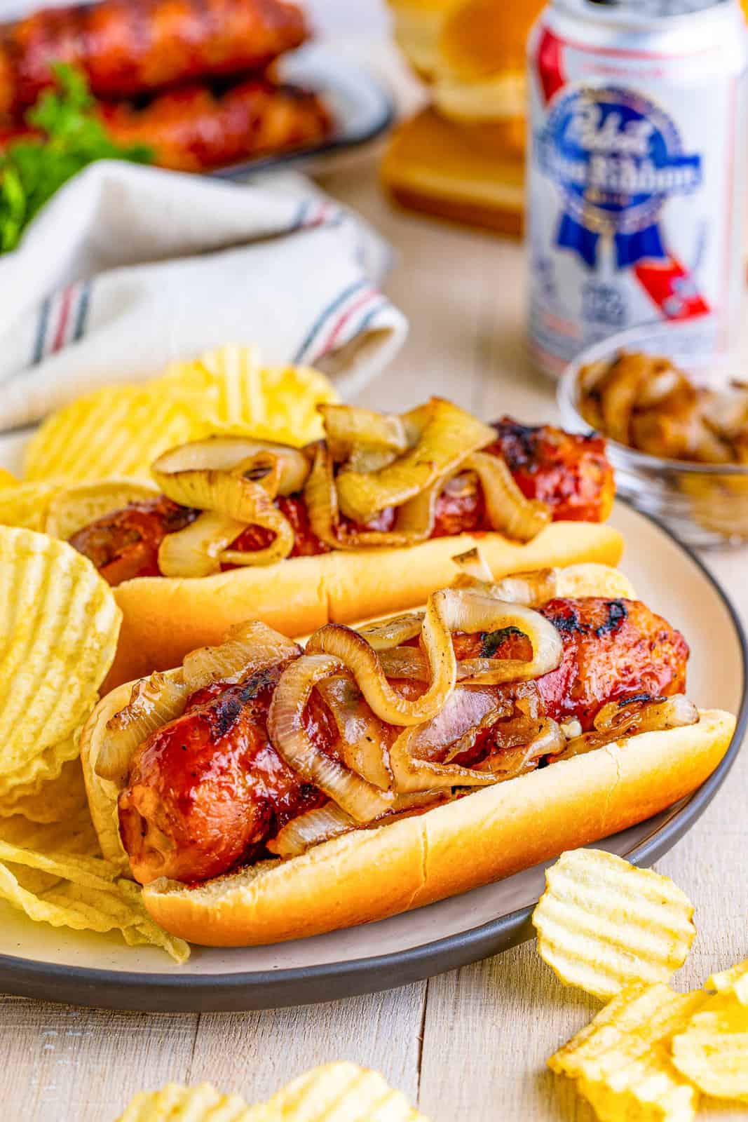 Cheese Stuffed Bacon Wrapped Brats on plate showing onions and chips.