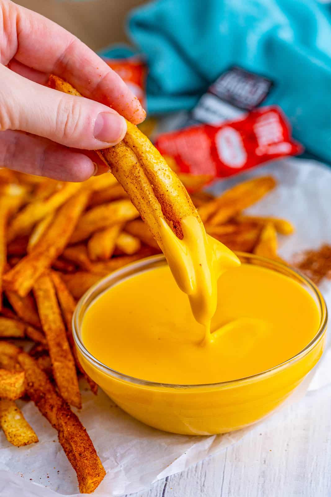 Hand dipping Taco Bell Nacho Fries into cheese sauce.