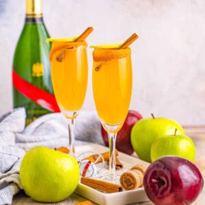 Square image of two Mimosas on plate with apples and champagne.