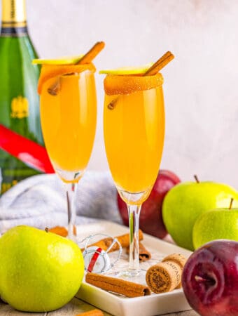 Square image of two Mimosas on plate with apples and champagne.