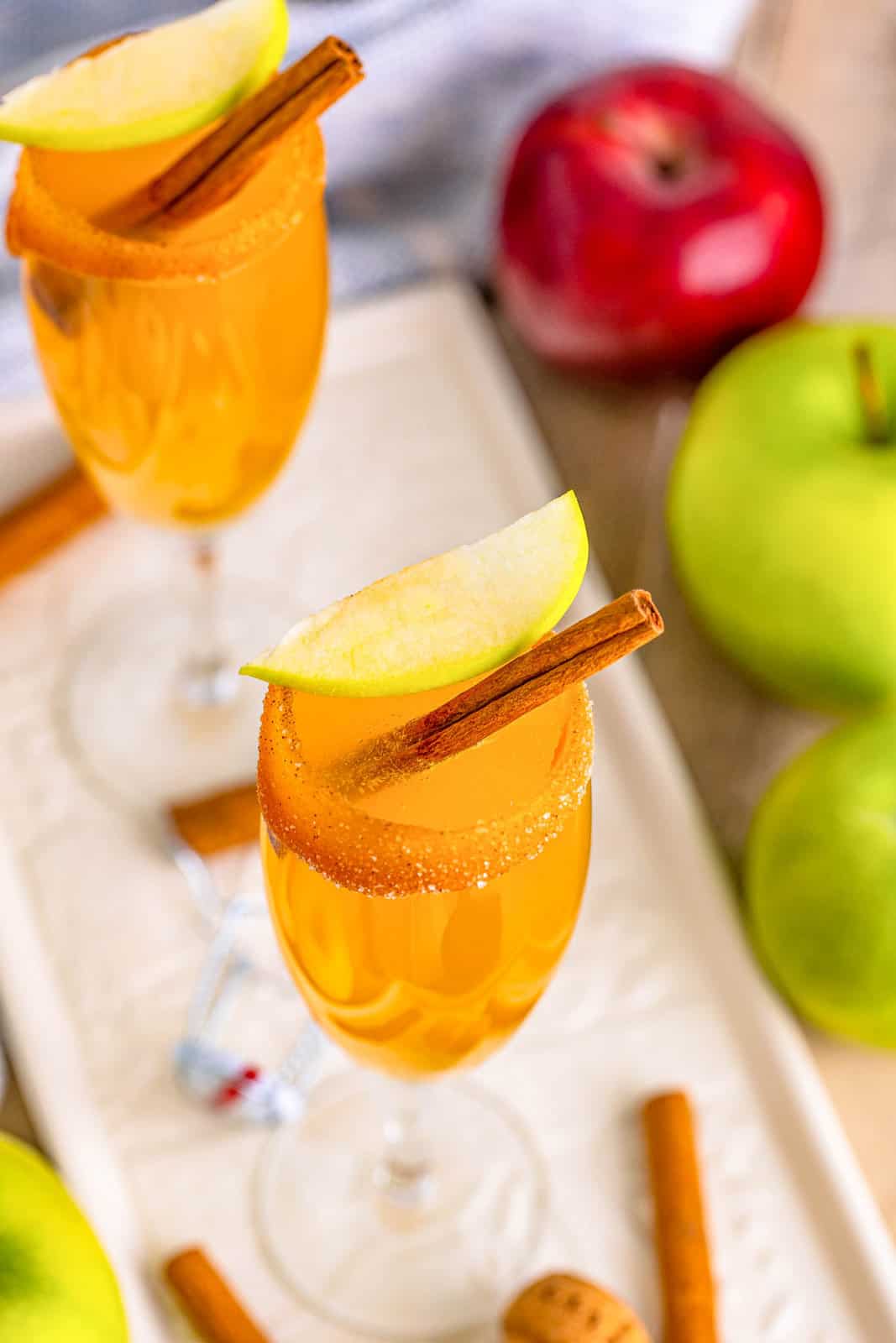 Overhead of Apple Cider Mimosas on white platter with apple and cinnamon garnish.