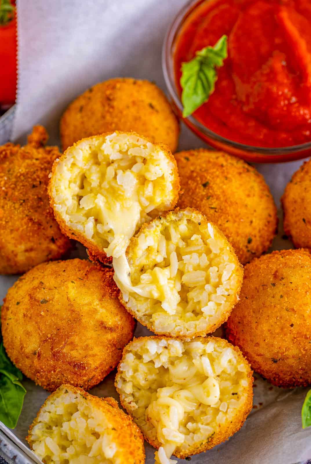 Arancini stacked on platter with one open showing cheesy inside.