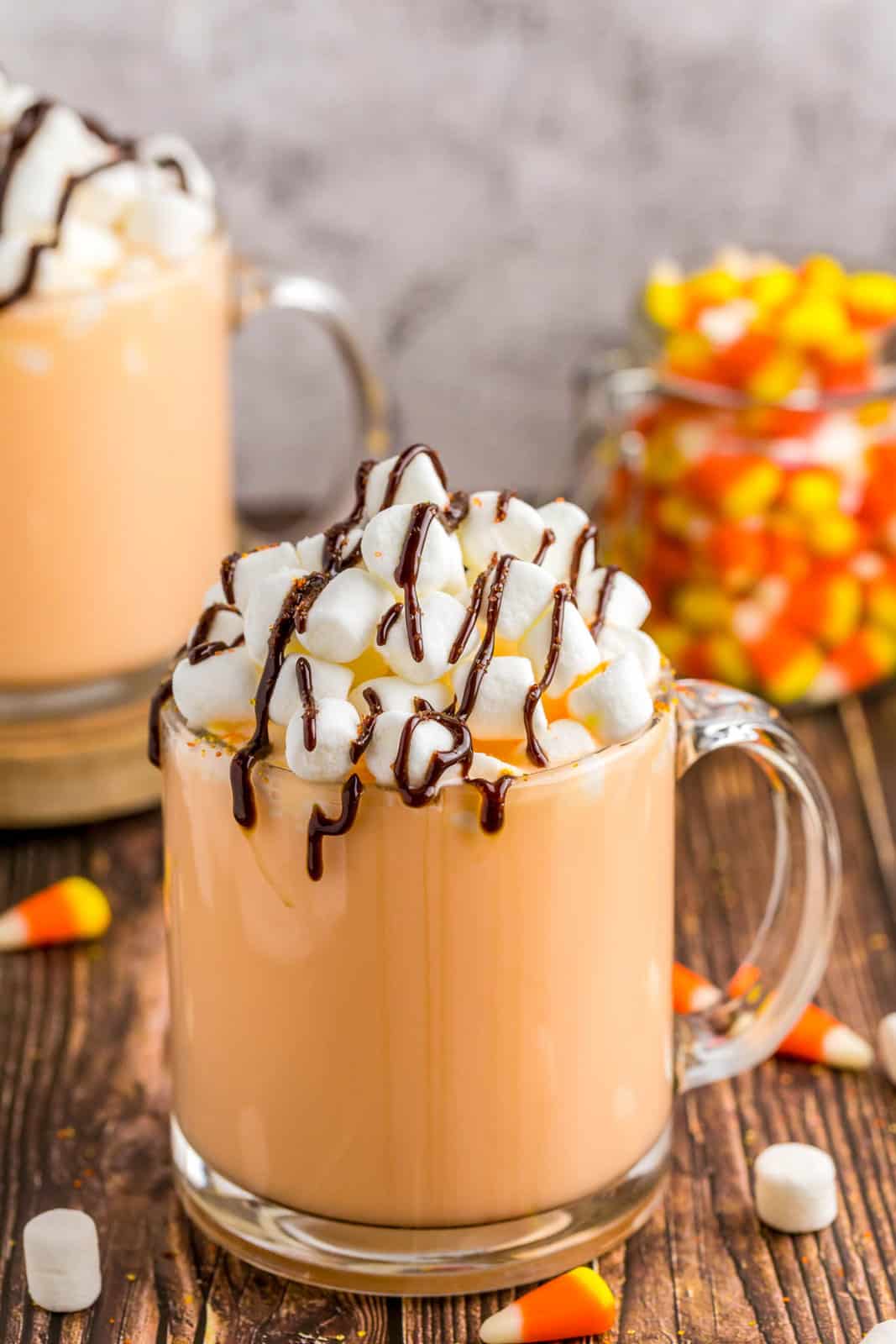 Close up of clear mug of Candy Corn Hot Chocolate garnished with candy corn in background.